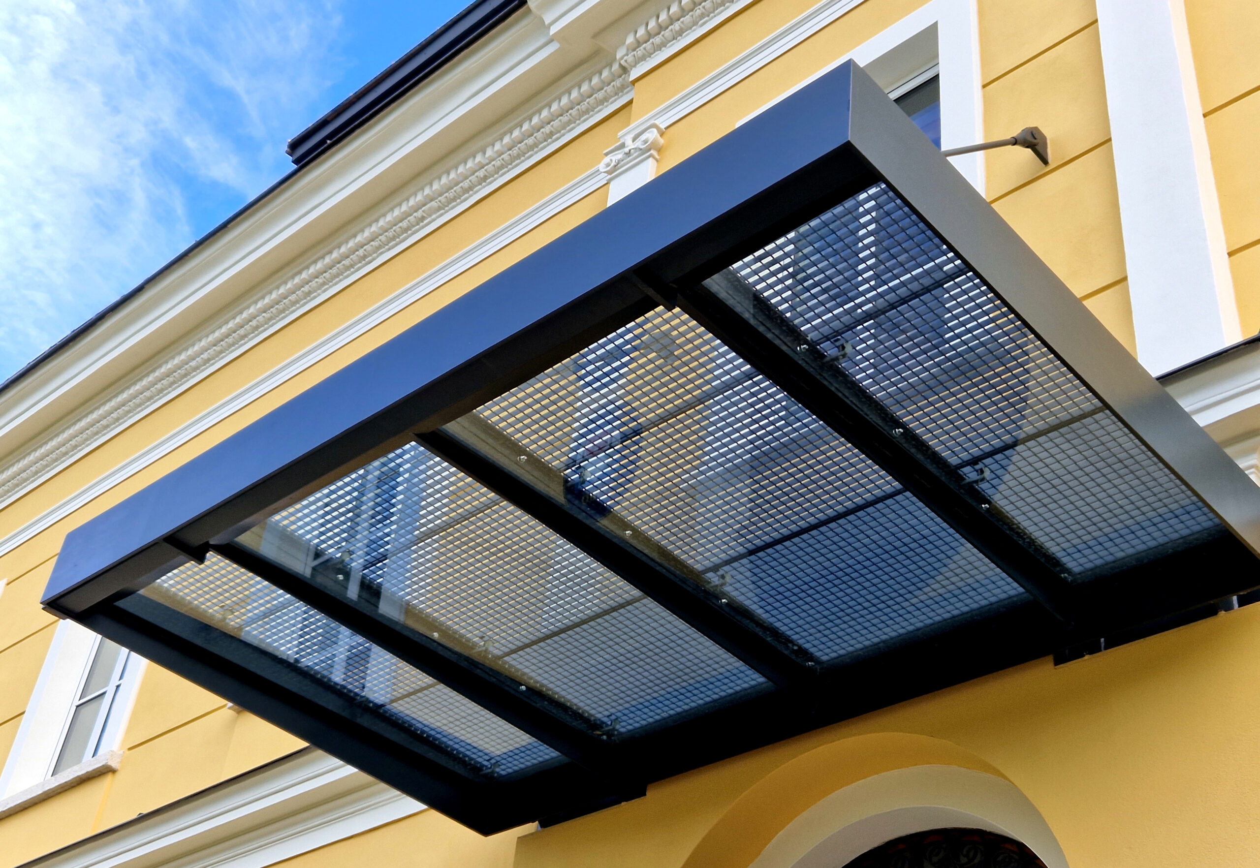 modern-looking glass roof suspended over the entrance to the town hall and school building. protection through sliding avalanches of snow and ice. metal grill above, window, struts, strutting