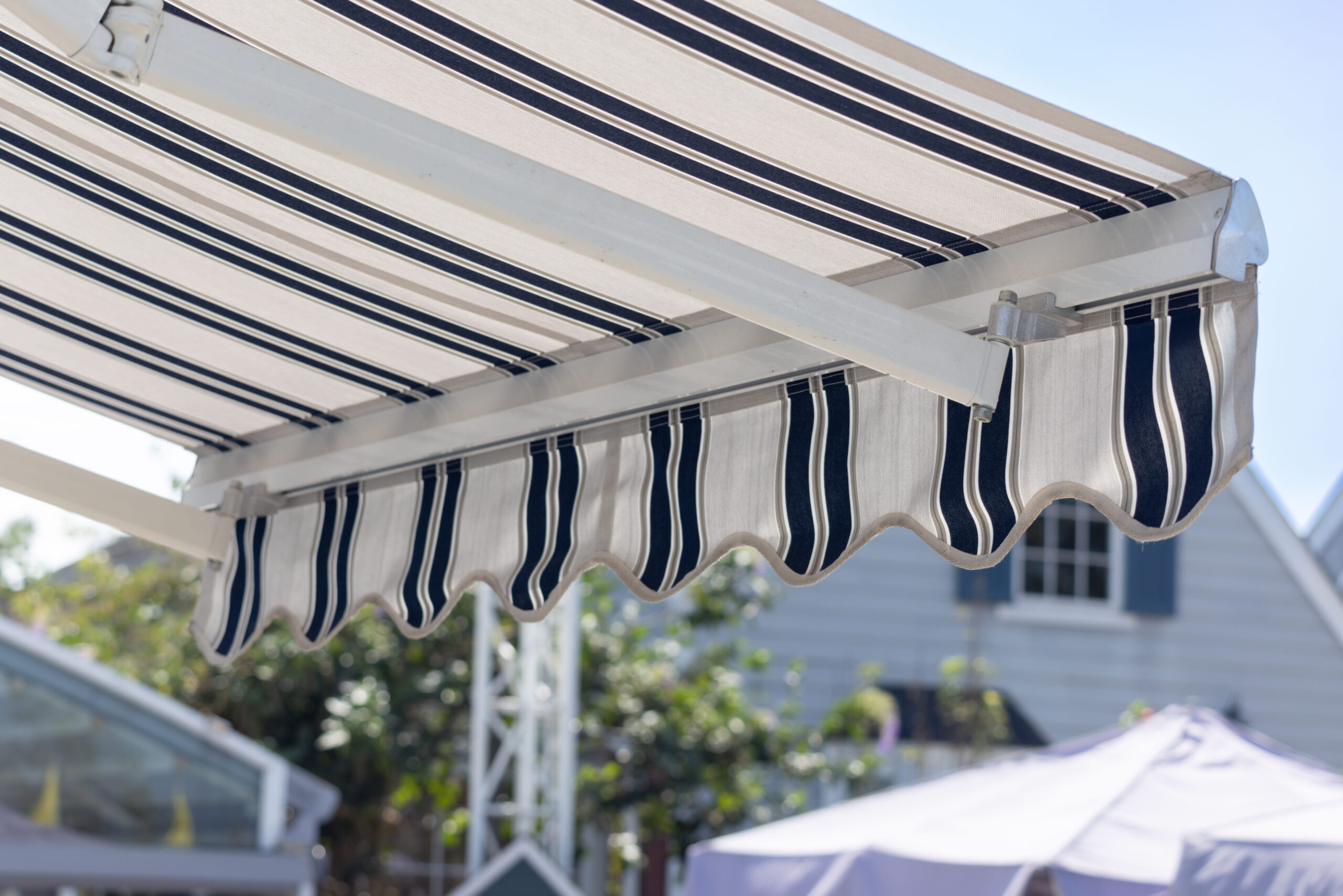 A blue and white striped awning is over a patio. The awning is open and the sun is shining on it